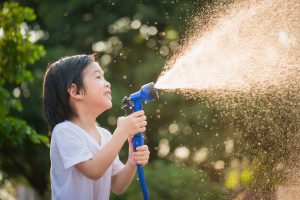 Cute asian boy has fun playing in water from a hose outdoors